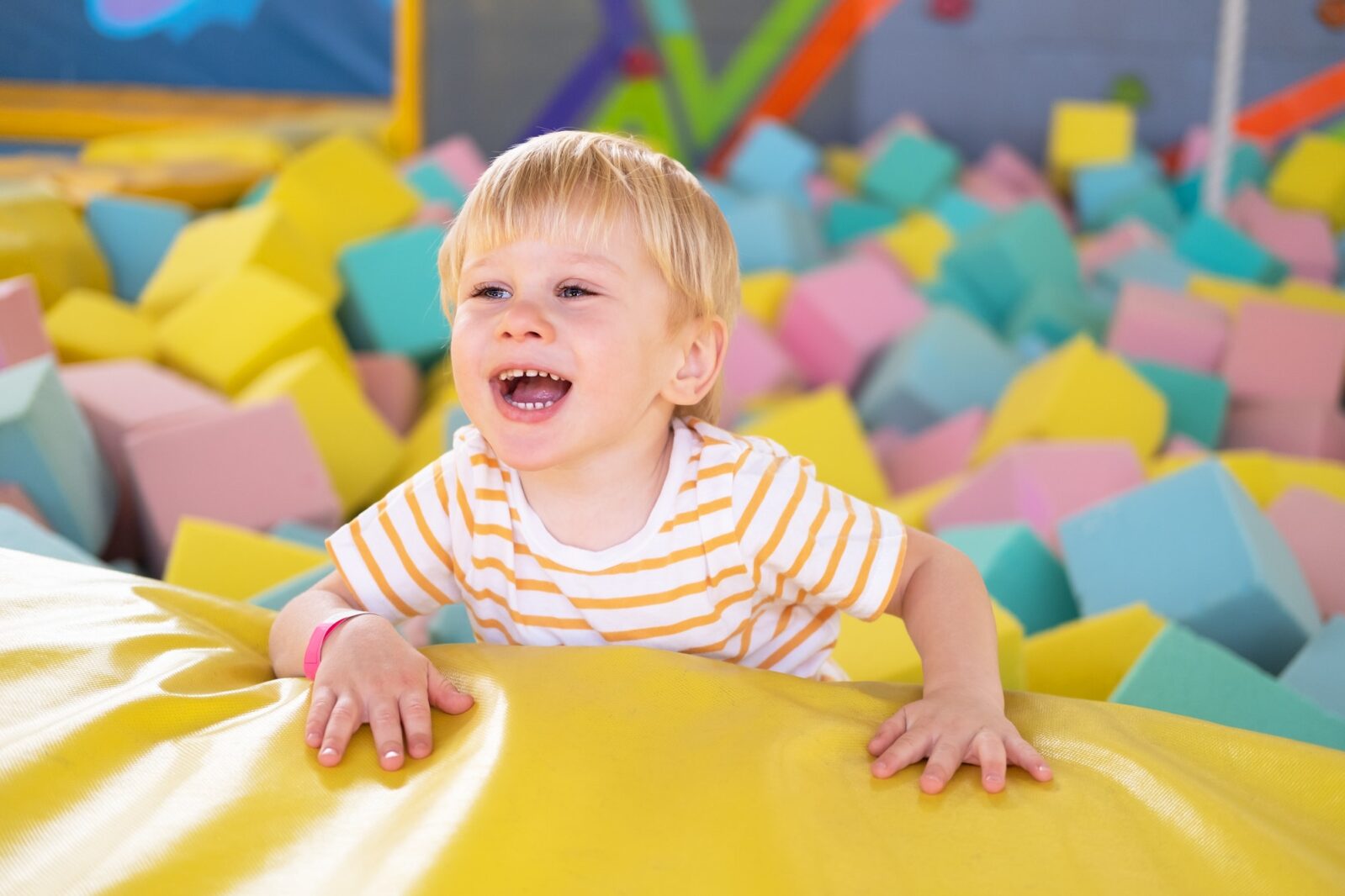 Cute smiling child boy plays with soft cubes in the dry pool in play center